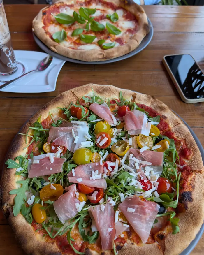 Pizza z szynką dojrzewającą, rukolą i pomidorkami na drewnianym stole